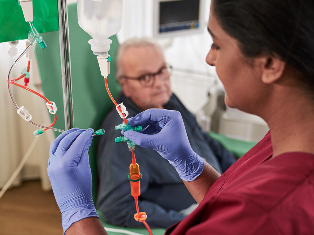Close-up of a provider wearing blue gloves using OnGuard CSTD to insert fluids into patient's IV.