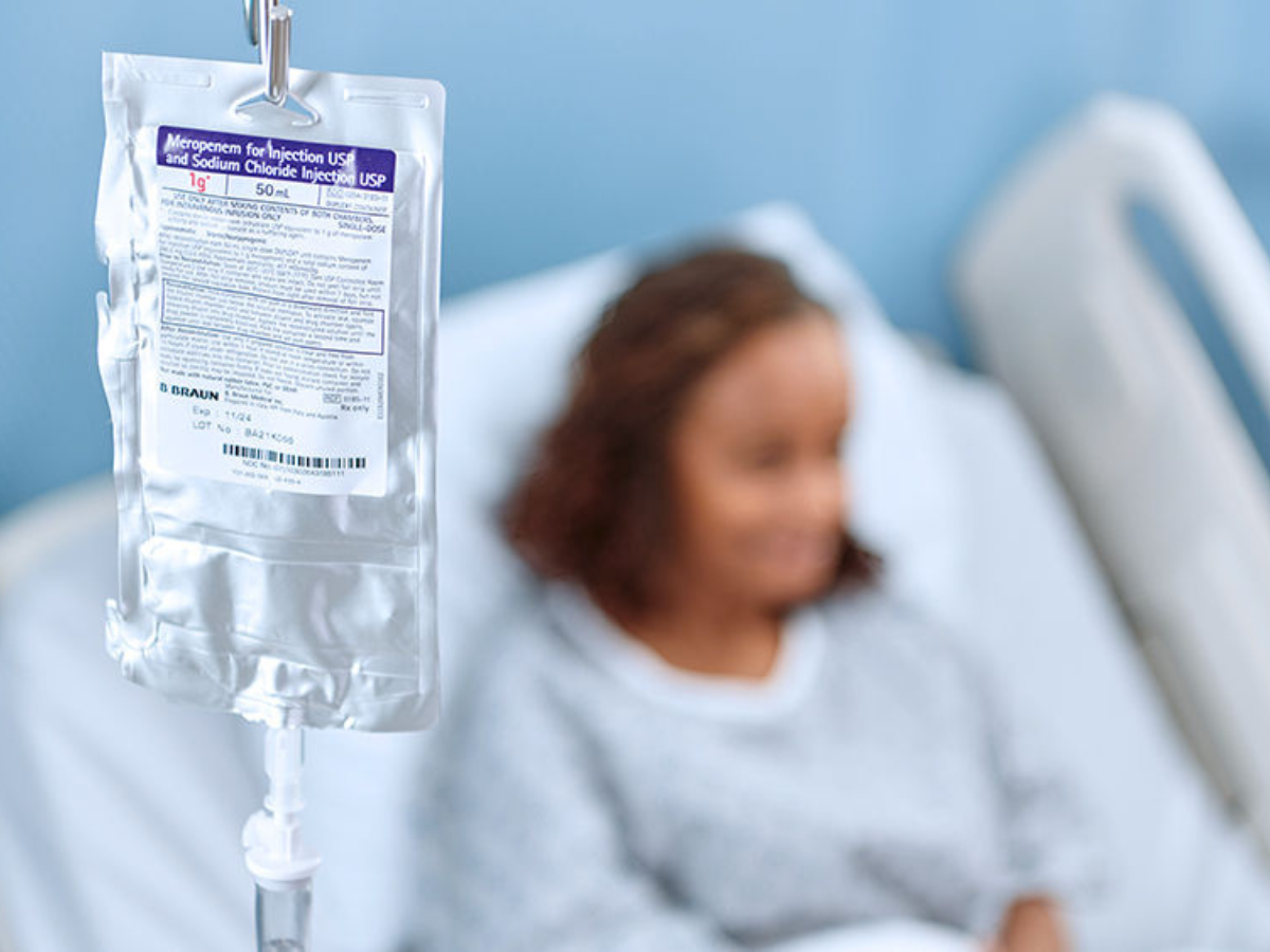 The innovative DUPLEX drug delivery system handing on an IV pole with the patient visible in the background lying on a hospital bed.