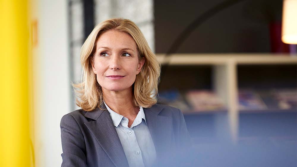 Une femme confiante en costume gris regarde devant l’appareil photo.  
